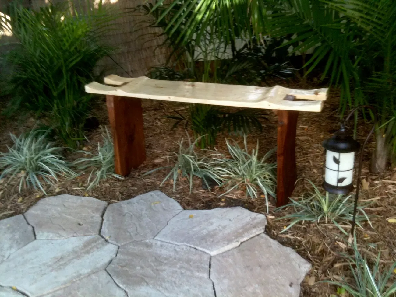 Live-edge bench on timber legs with a laid flagstone path.