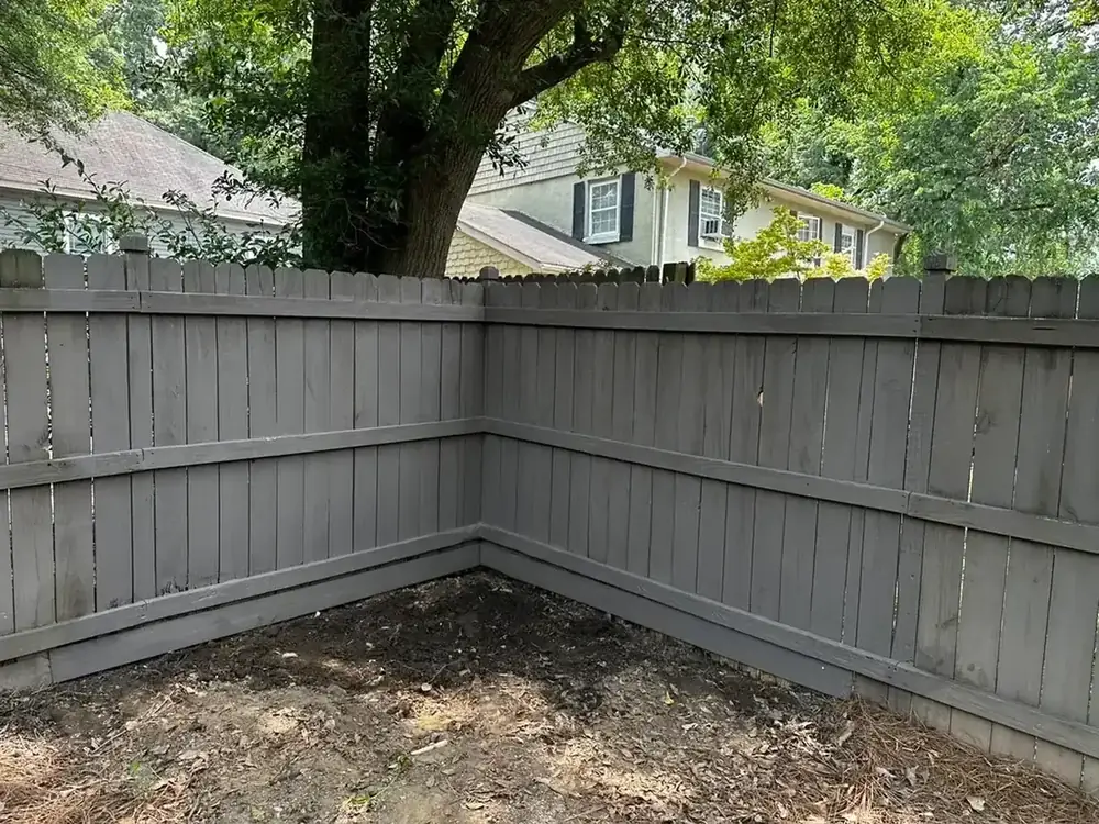 A weathered grey privacy fence at a back-yard corner before repair