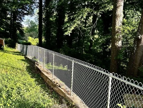 A sagging chain-link fence running down a wooded slope before replacement