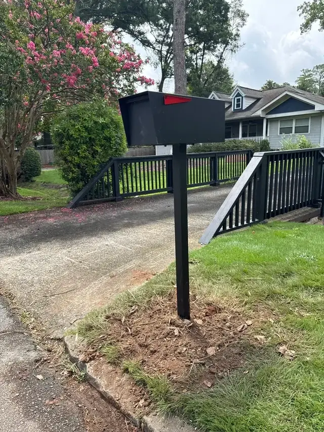 A newly installed black mailbox on a post at the end of a driveway